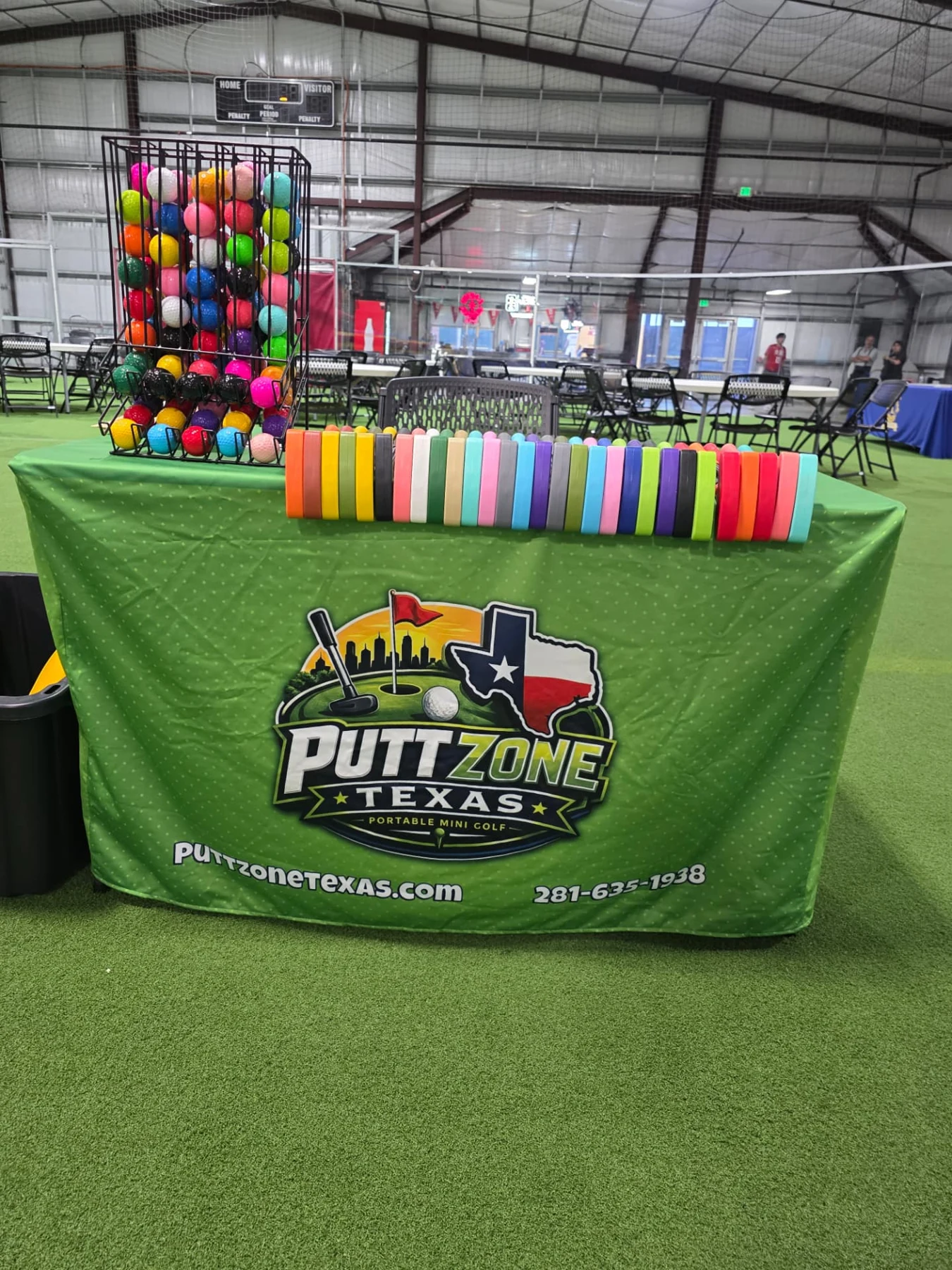 Colorful putters and golf balls on a table with the Putt Zone Texas branded banner