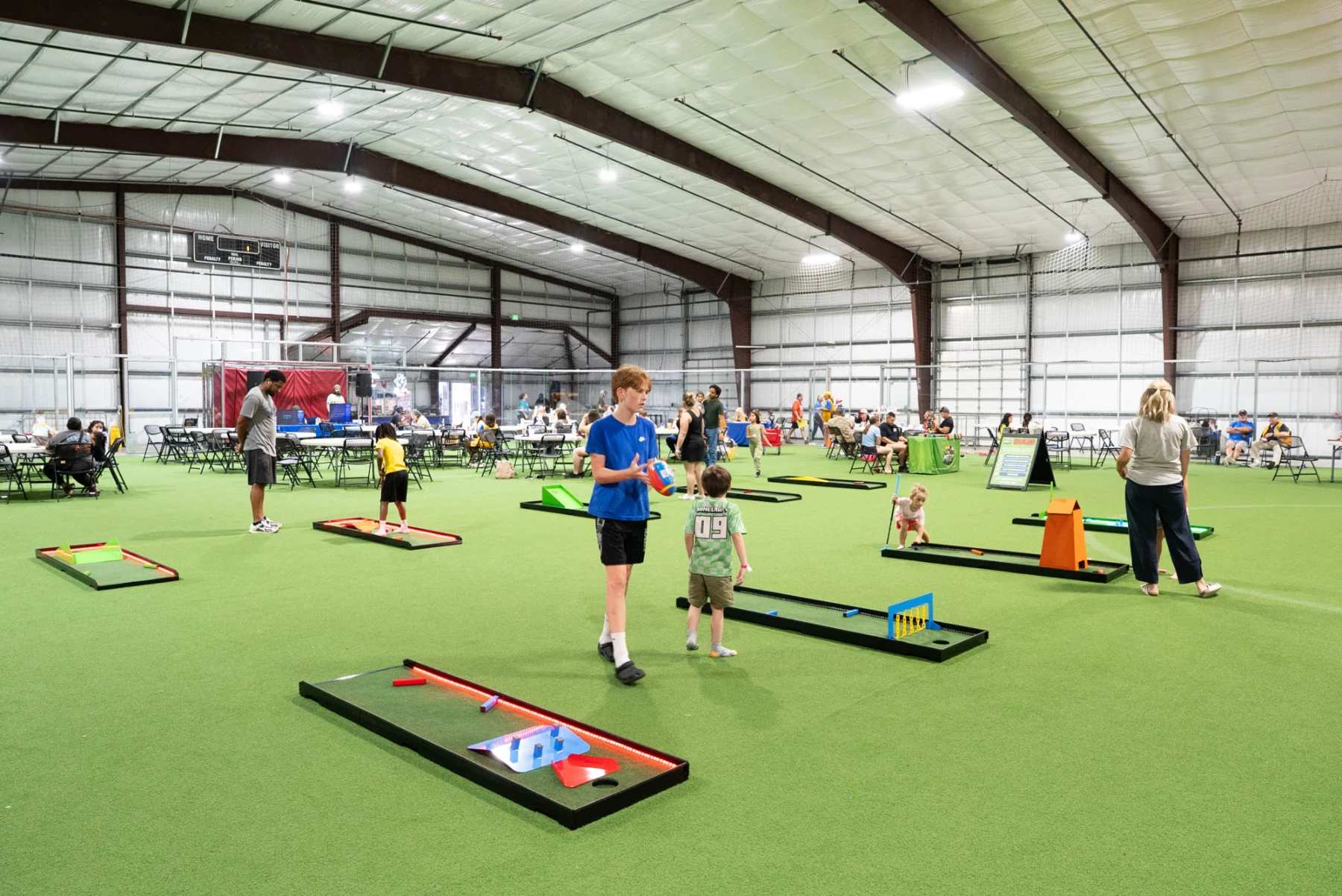 Children and adults playing the Putt Zone Texas portable mini-golf course on indoor turf